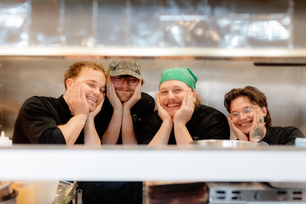 Three friends smiling into an open refrigerator