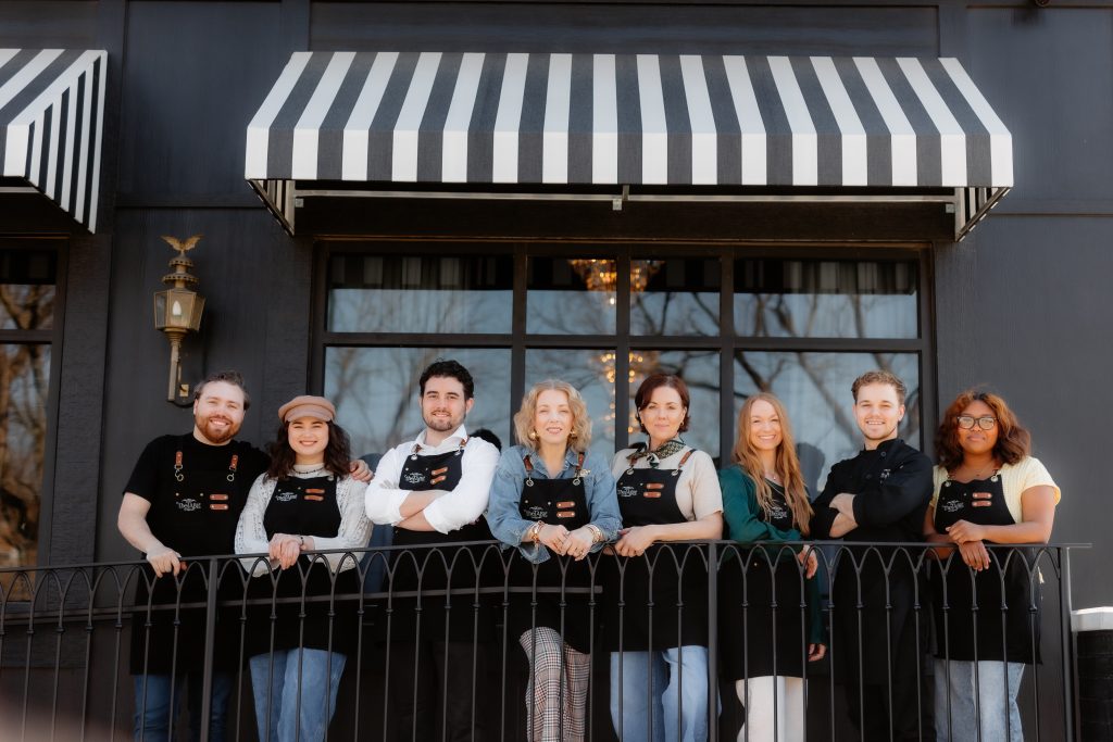 Smiling restaurant staff pose on balcony outside dark storefront